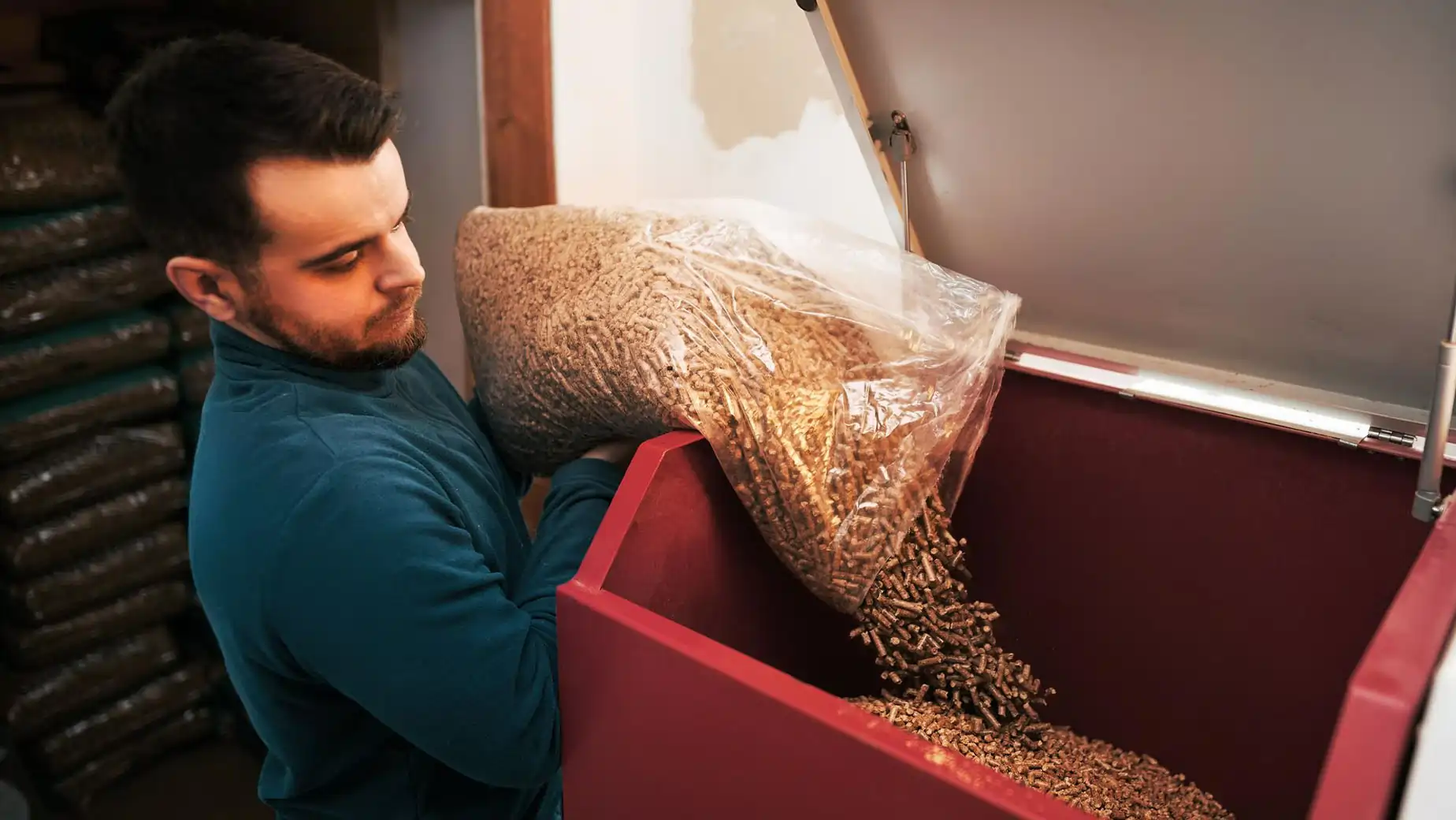 Facet w niebieskim swetrze wsypujący certyfikowany pellet do kotła na pellet 5 klasy dostępnego na dofinansowanie z programu Czyste Powietrze